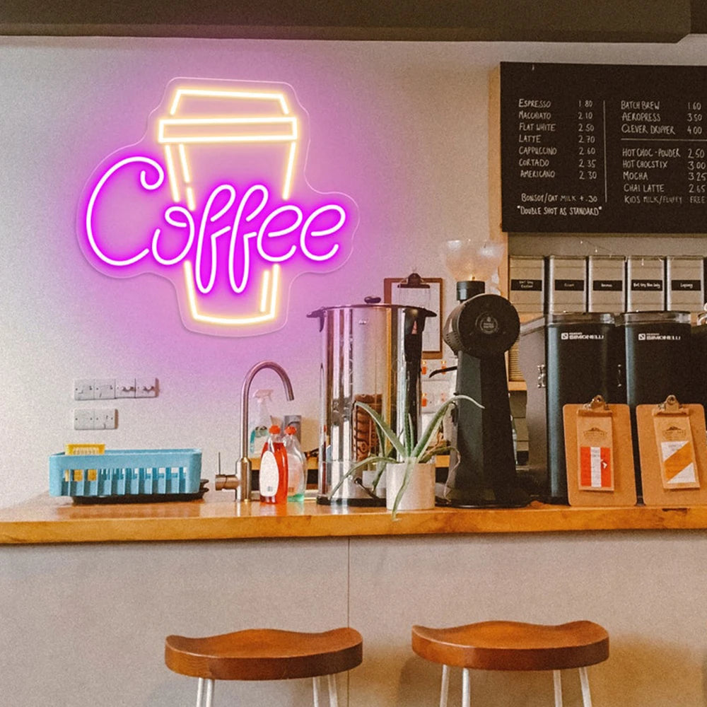 Neon 'Coffee' sign above a counter with coffee-making equipment and stools in a coffee shop.