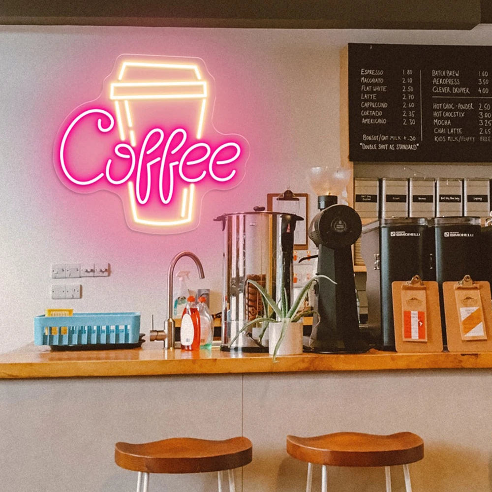 Neon 'Coffee' sign above a counter with coffee-making equipment and stools in a cafe.
