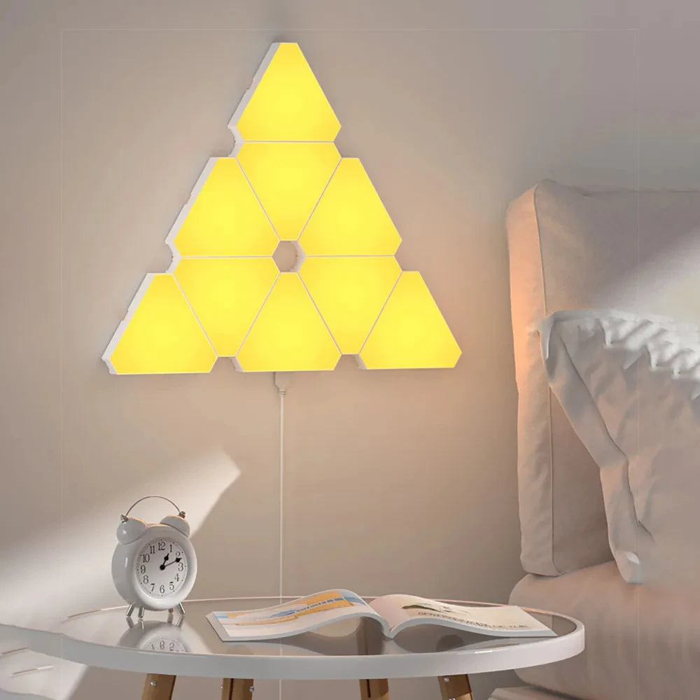 Triangular LED wall light fixture in a bedroom setting with a table and alarm clock.