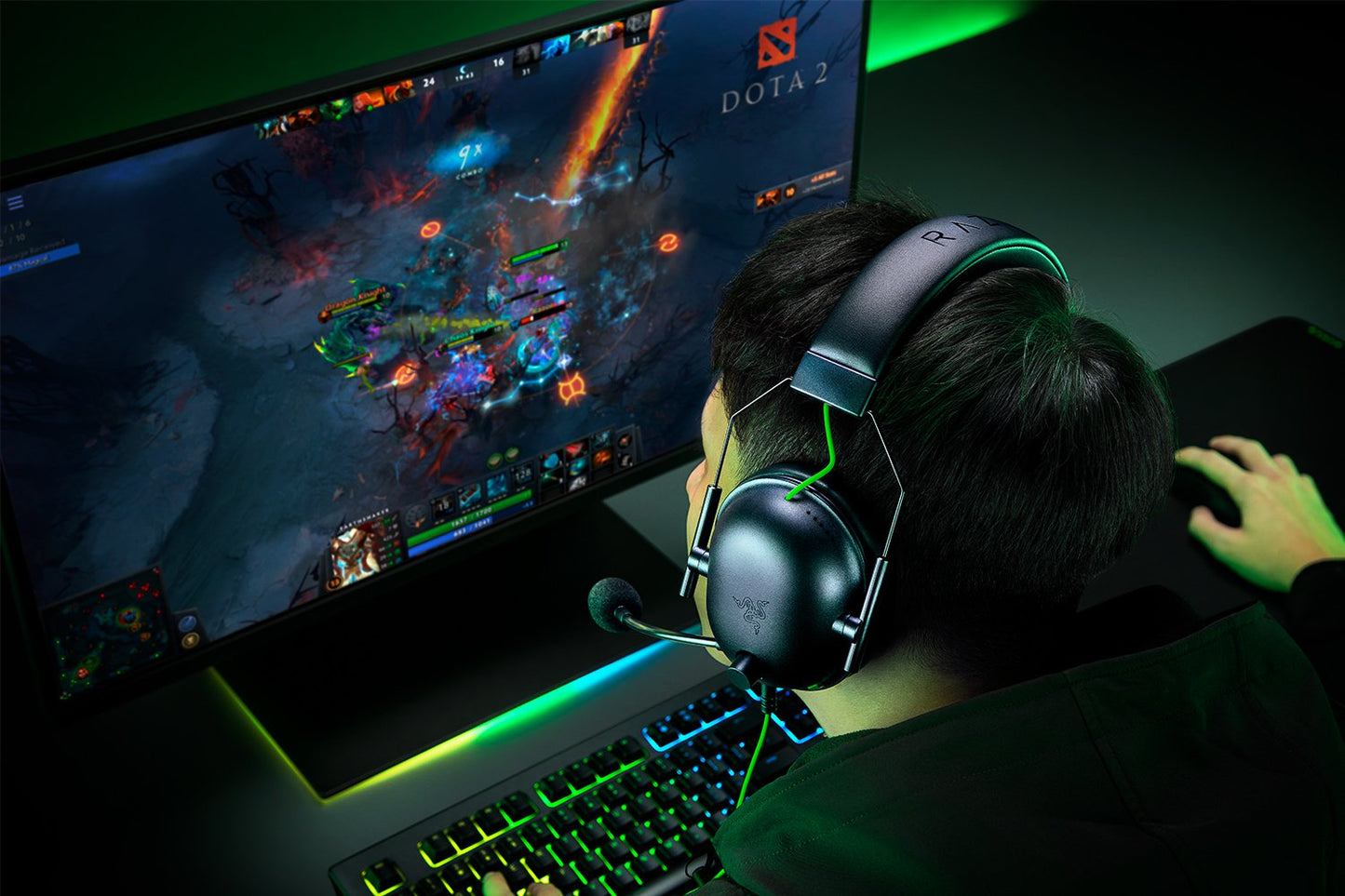 Person playing a game on a computer with headphones, surrounded by gaming equipment.