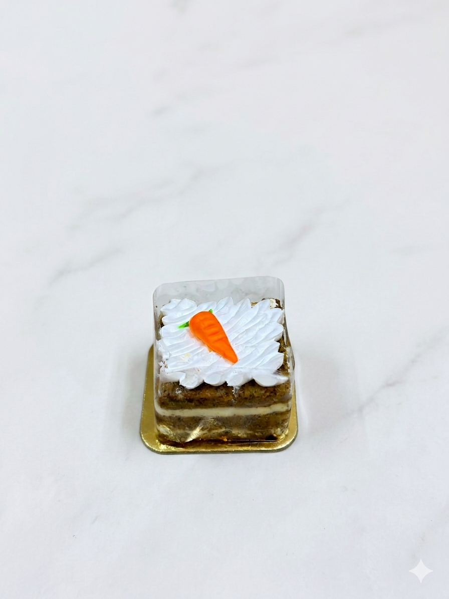 Small carrot cake with white frosting and a single carrot on top, placed on a white surface.