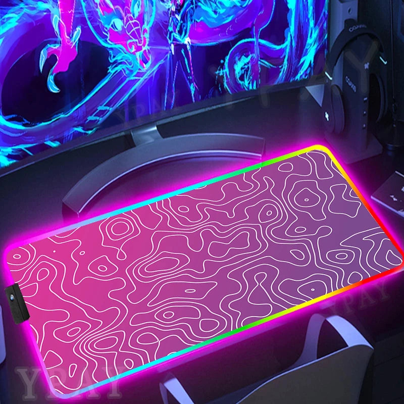 Gaming desk setup with a large RGB illuminated mouse pad, monitor, and headphones.