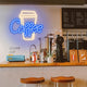 Neon coffee cup sign above a counter with coffee-making equipment and stools in a coffee shop.