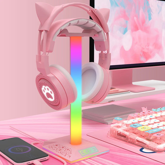 Pink gaming headset with cat ears on a desk with a colorful lamp and keyboard.