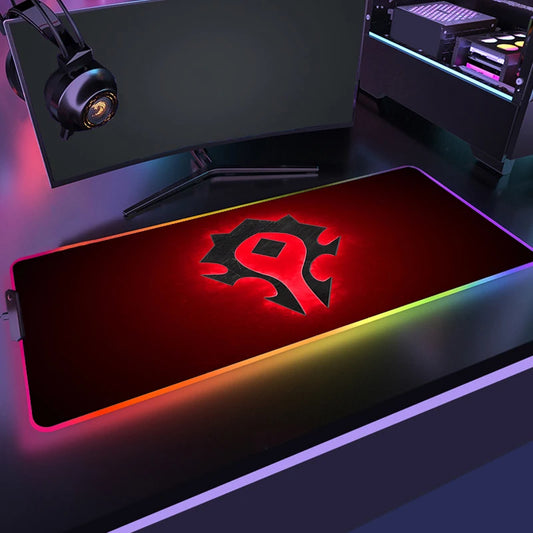 Gaming desk setup with a large mouse pad featuring a logo, monitor, and RGB lighting.
