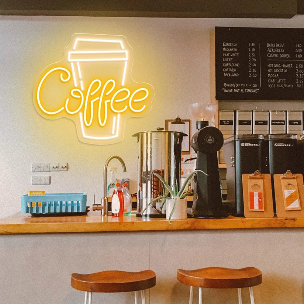 Neon coffee sign above a counter with coffee-making equipment and stools in a coffee shop.