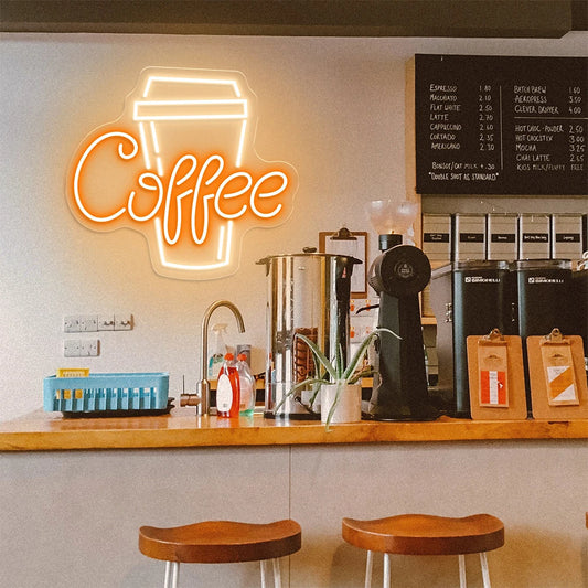 Neon coffee sign above a counter with coffee-making equipment and stools in a coffee shop.