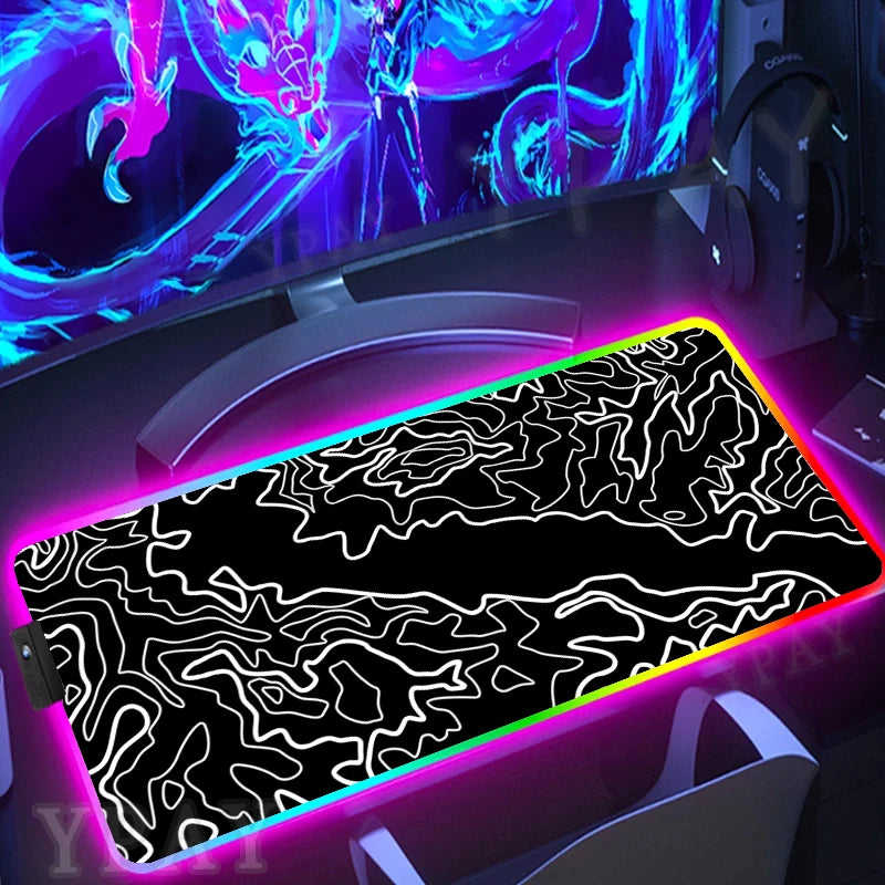 Gaming desk setup with a large mouse pad featuring a black and white abstract design, illuminated by colorful LED lights.