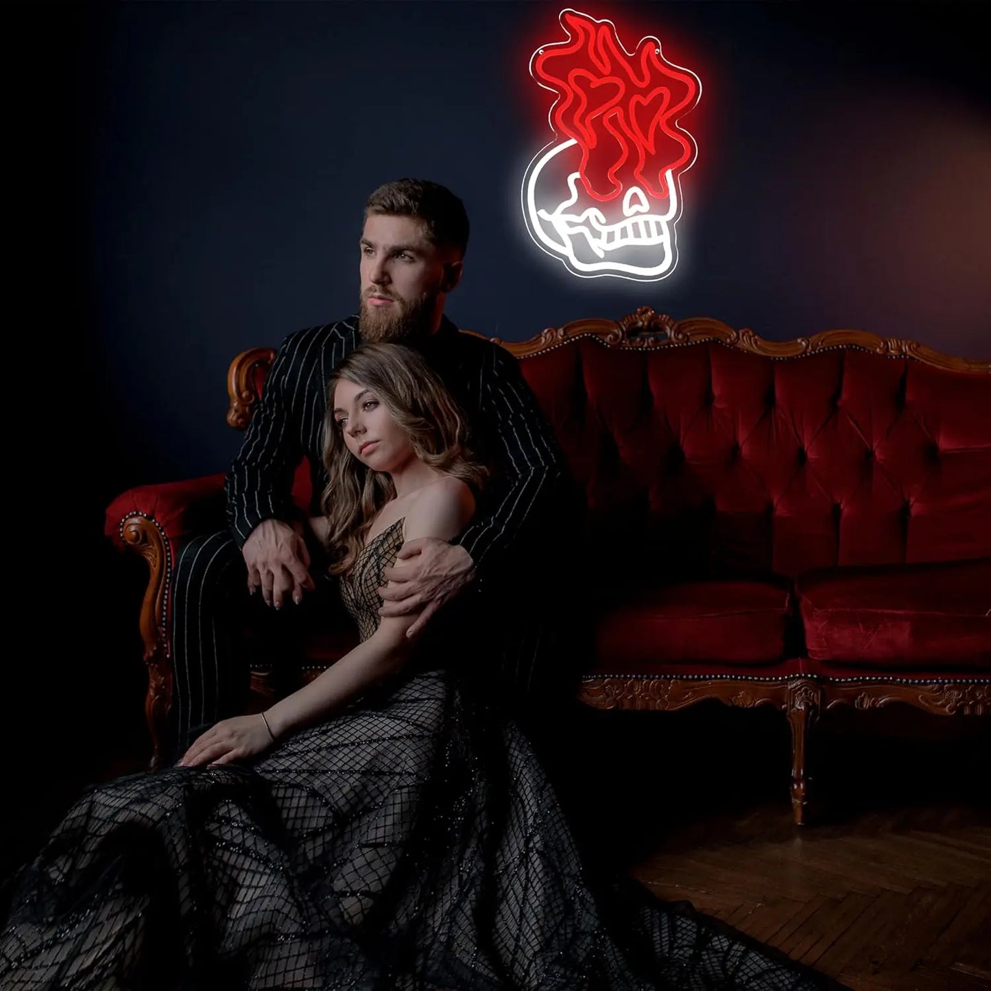 Man and woman sitting on a red couch with a neon sign above them