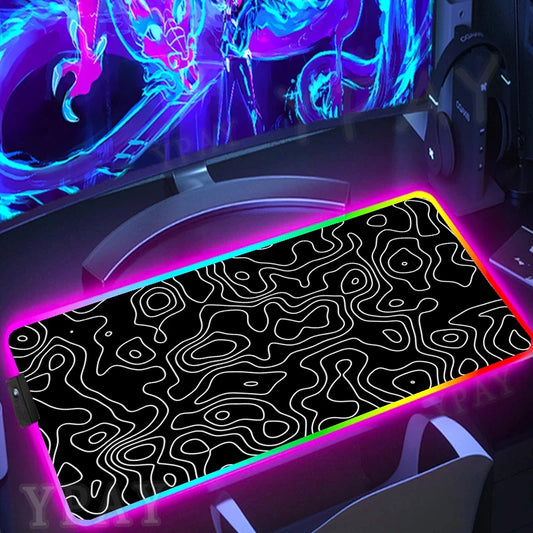 Gaming desk setup with a large mouse pad featuring a black and white pattern, illuminated by colorful lights.